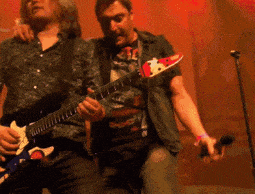a man playing a guitar next to another man playing a microphone