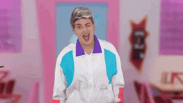 a woman wearing a wig and a colorful jacket is standing in a pink room .