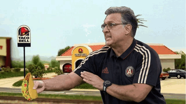 a man in an adidas shirt is throwing a taco in front of a taco bell