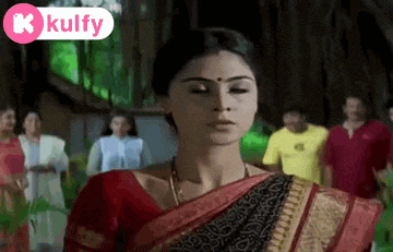 a woman in a red and black saree stands in front of a group of people .