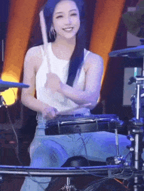 a woman in a white tank top is playing drums while sitting on a drum set .