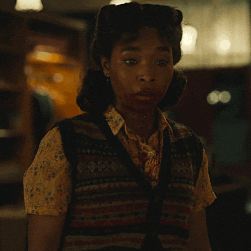 a woman with blood on her face is wearing a sweater vest and a yellow shirt