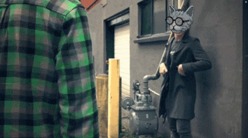 a man in a green plaid shirt stands next to a woman with a cat mask on her head
