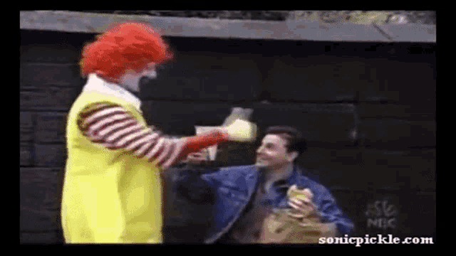 a mcdonald 's clown is giving a man a hamburger while another man holds a bag of chips