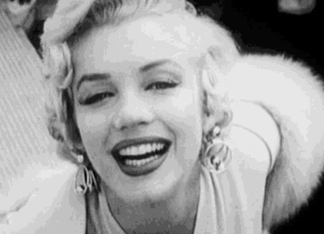 a black and white photo of a smiling woman wearing earrings and a fur collar .