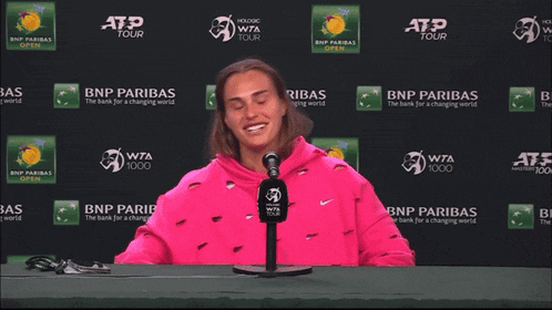a woman in a pink sweatshirt is sitting in front of a bnp paribas sign