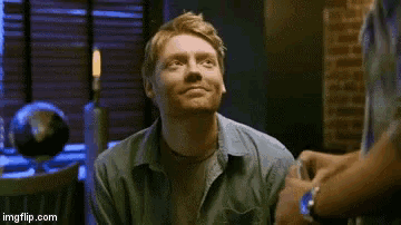 a man in a blue shirt is smiling while sitting in a chair in a room .