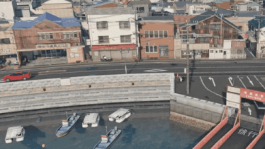 a red car is driving down a street in front of a building that says ' aoyama ' on it