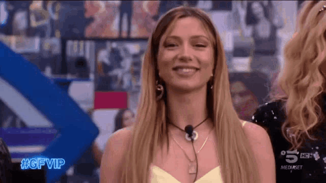 a woman in a yellow top is smiling in front of a microphone on a tv show .