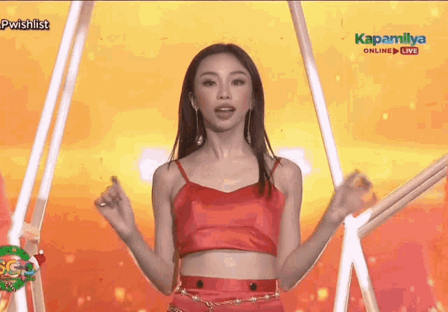 a woman in a red crop top is dancing on a stage in front of a yellow background .