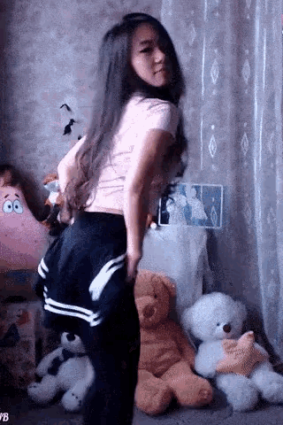 a woman in a pink shirt is dancing in front of stuffed animals including a spongebob pillow