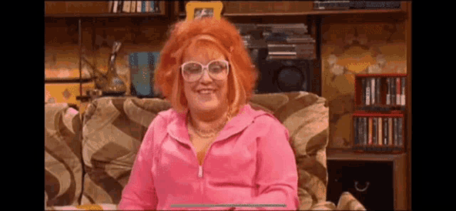 a woman with red hair and glasses is sitting on a couch in a living room .