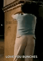 a woman in a blue shirt and white pants is standing in front of a building and says `` love you bunches '' .