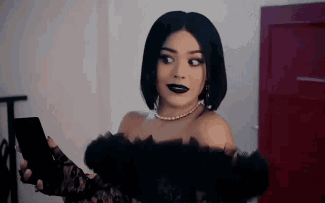 a woman in a black dress and black lipstick is looking at herself in the mirror .
