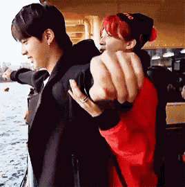 a man in a black jacket is carrying another man in a red jacket on his back .