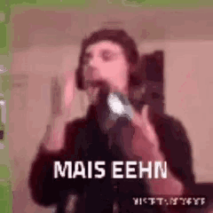 a man wearing headphones is singing into a microphone with the words `` mais eehn '' written on the screen .