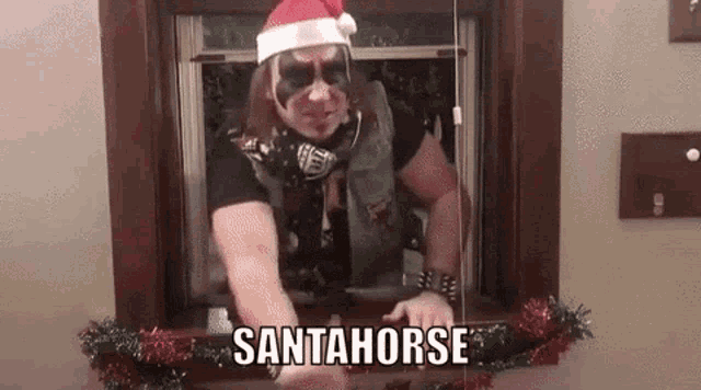 a man in a santa hat is standing in front of a window and says santahorse .