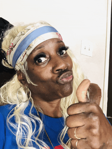 a woman with blonde hair wearing a headband and earrings giving a thumbs up