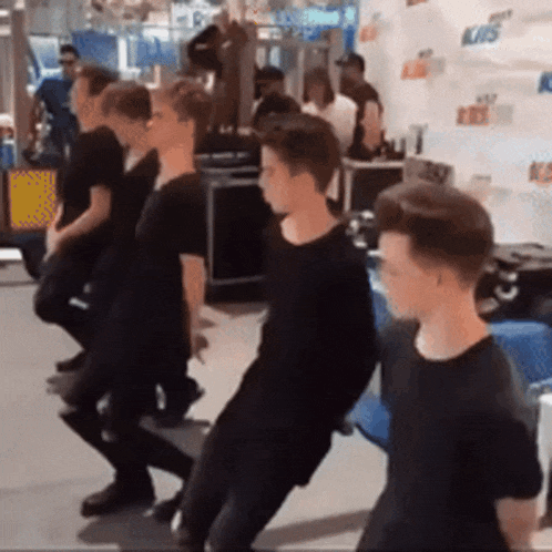 a group of young men in black shirts are dancing in front of a wall that says kiss on it
