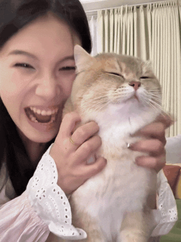 a woman is holding a cat with her eyes closed and smiling