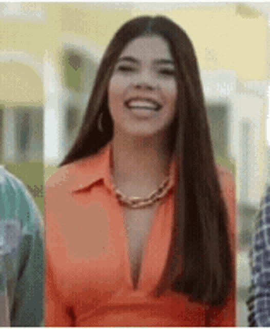 a woman in an orange shirt and necklace is smiling .