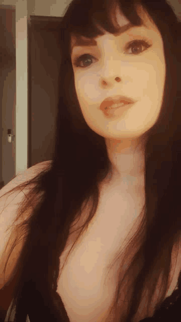 a woman with long black hair and a plunging neckline looks at the camera