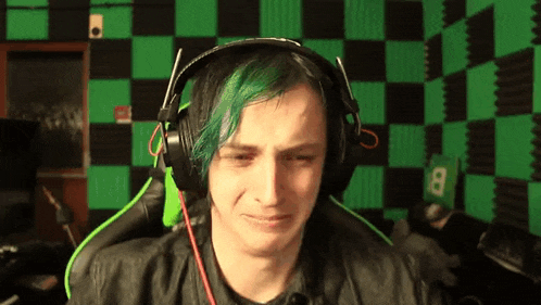 a man with green hair wearing headphones is crying in front of a green and black checkered wall .