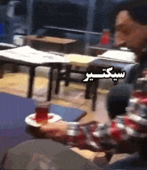 a man is sitting at a table with a cup of tea in front of him with arabic writing on it