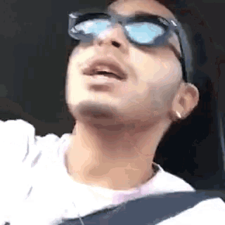 a man wearing sunglasses is driving a car and looking up .