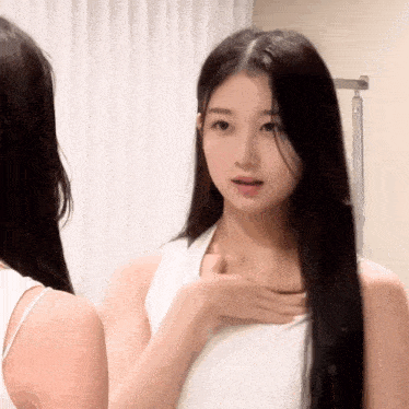 a woman with long black hair is looking at herself in a mirror