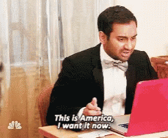 a man in a suit and bow tie is sitting at a desk with a laptop and says " this is america i want it now "