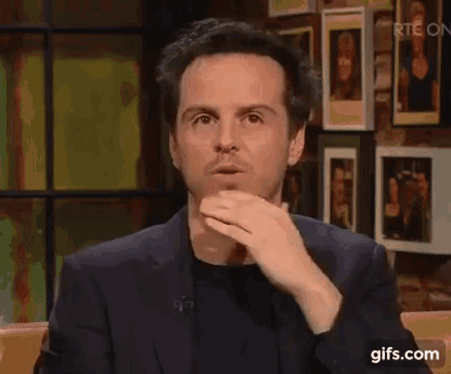 a man in a suit and black shirt is sitting on a couch .