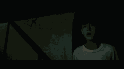 a young boy in a white shirt is standing in the dark .