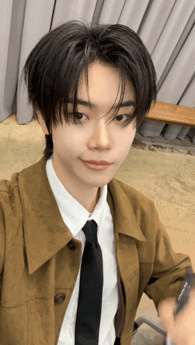a young man wearing a brown jacket and black tie taking a selfie