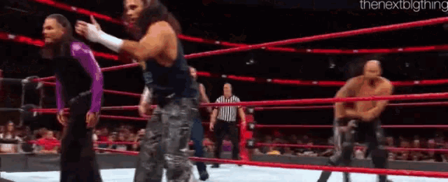 a group of wrestlers are standing in a wrestling ring with a referee watching .