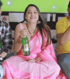 a woman in a pink saree is holding a green bottle of beer