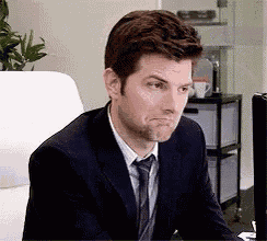 a man in a suit and tie is sitting at a desk making a face .