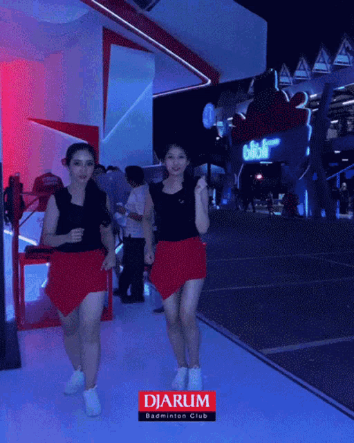 two women in red skirts are dancing in front of a sign that says djarum badminton club
