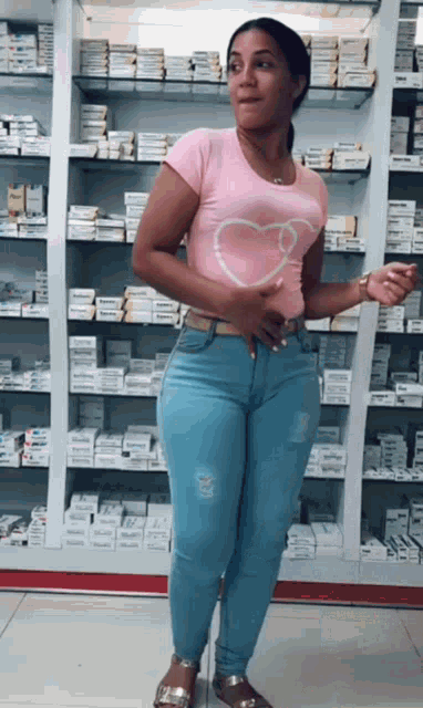 a woman in a pink shirt with a heart on it stands in front of a pharmacy shelf