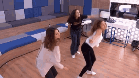 three women are dancing in a room with a sign that says g on it
