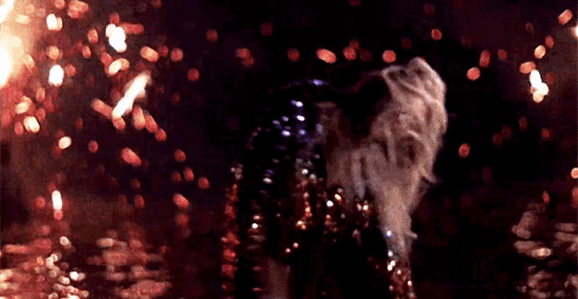 a woman in a sequined dress is standing in front of a fire at night