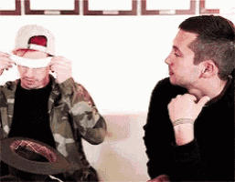 two men are sitting on a couch and one of them is putting a bandage on his face .