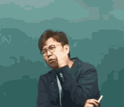 a man wearing glasses and a suit is sitting in front of a blackboard .
