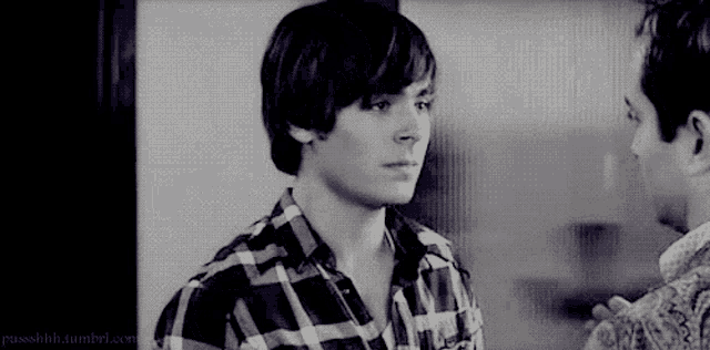 a man in a plaid shirt is talking to another man