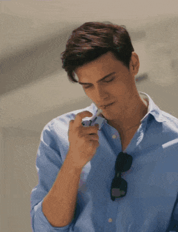 a man wearing a blue shirt and sunglasses is smoking an electronic cigarette