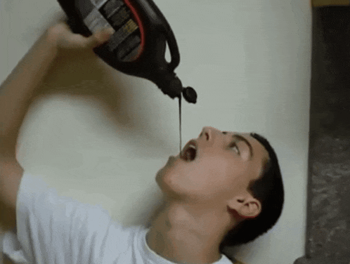 a young man is drinking from a bottle that has a warning label