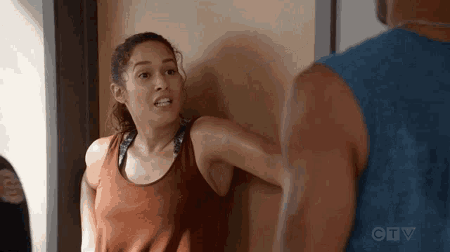 a woman in a tank top is leaning against a wall while a man in a blue tank top stands behind her .
