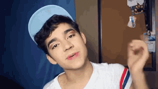 a young man wearing a blue hat and a white shirt looks at the camera