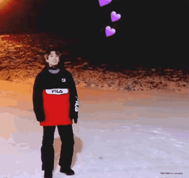a person is standing in the snow wearing a red and black fila jacket .