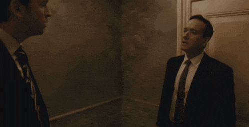 a man in a suit and tie is walking down a dark hallway